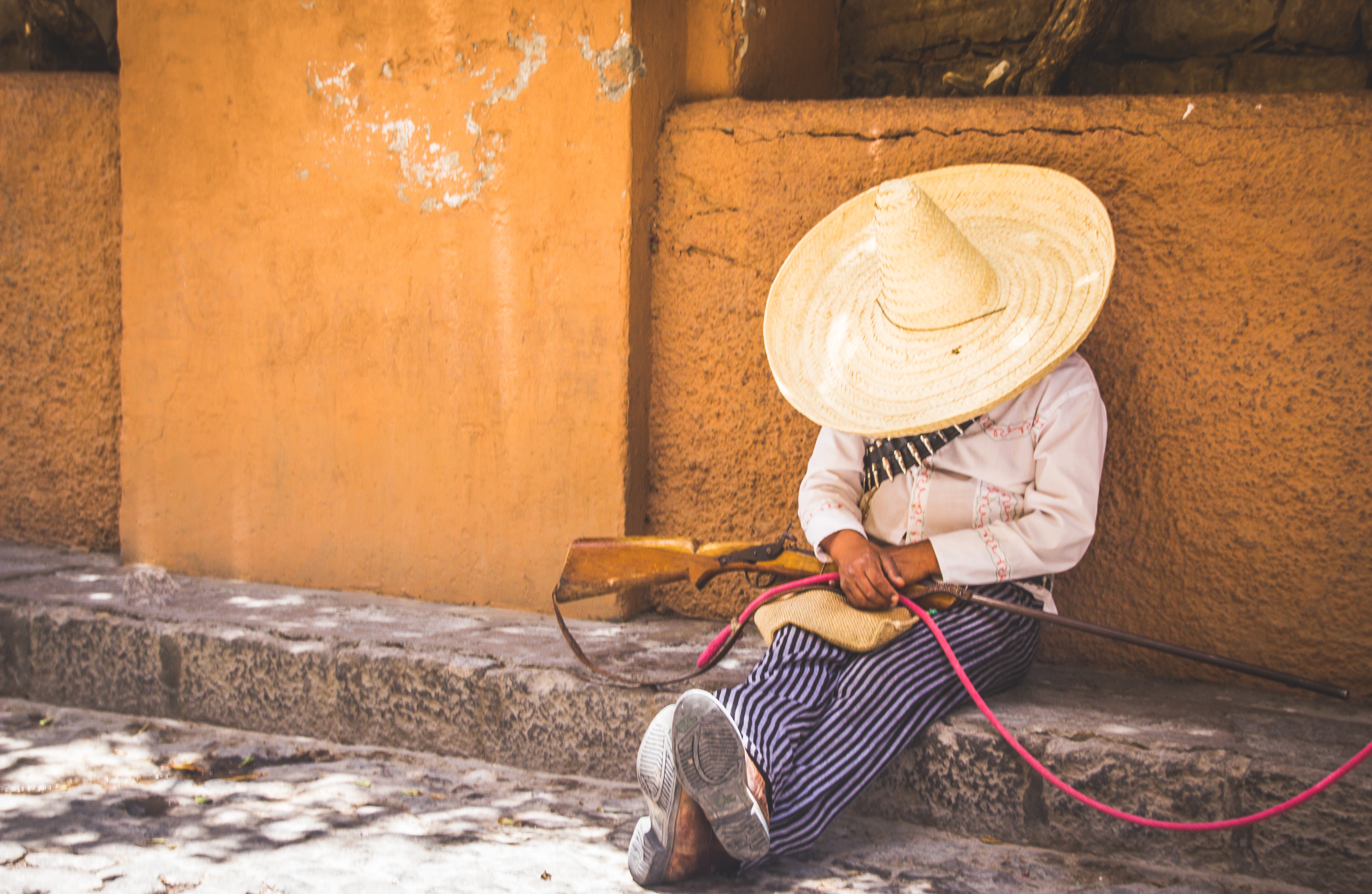 Man wearing sombrero sitting against a wall