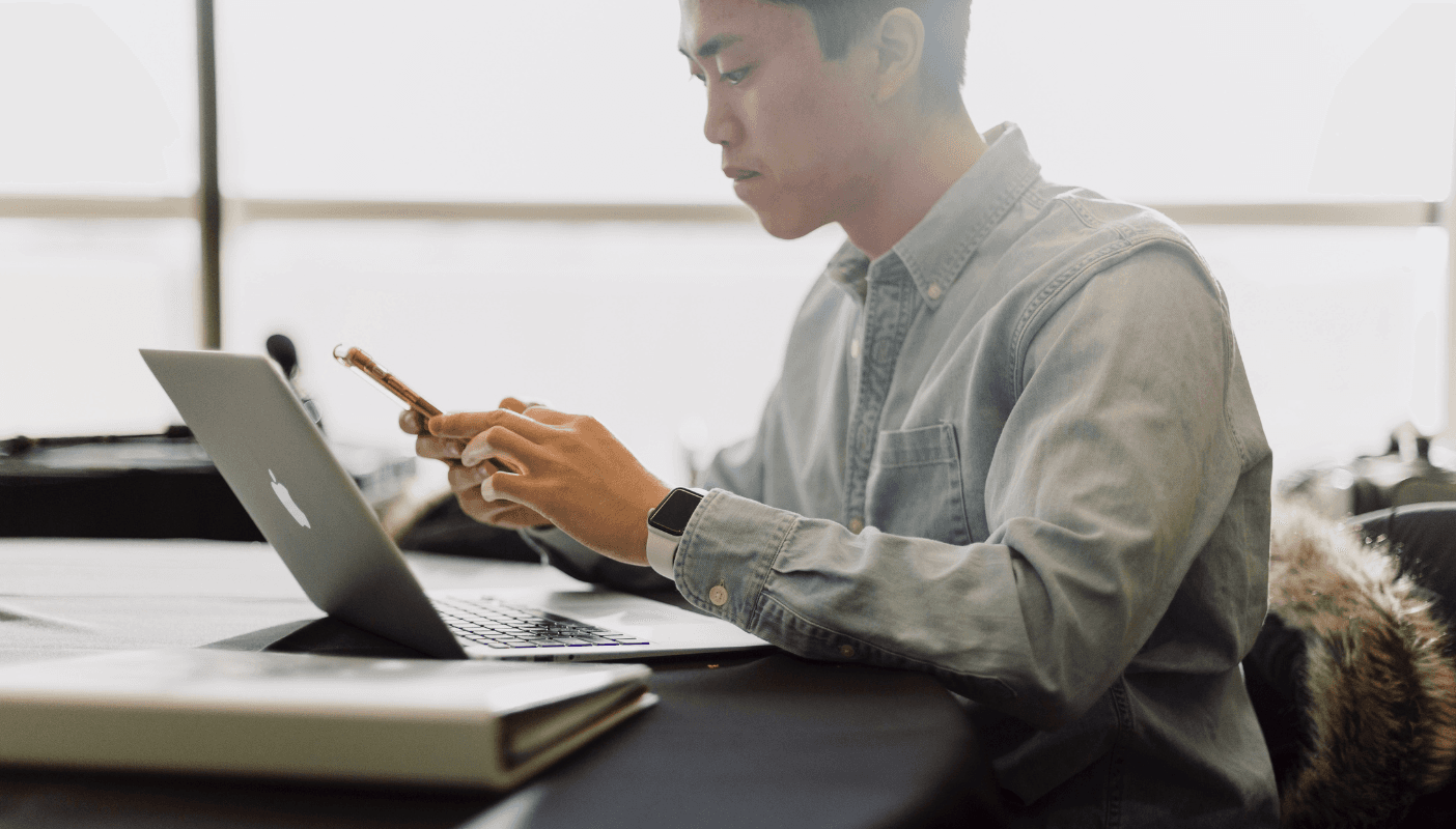 Man looking at phone and using computer